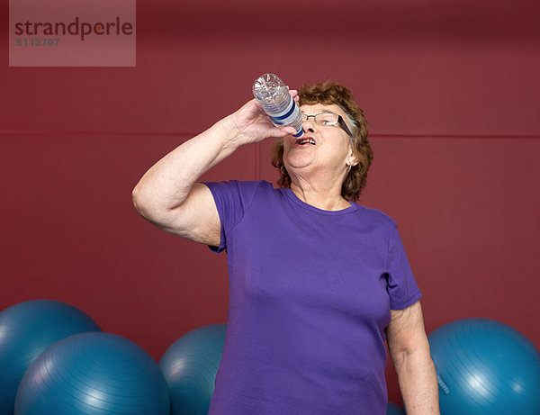 Ältere Frau trinkt Wasser im Fitnessstudio