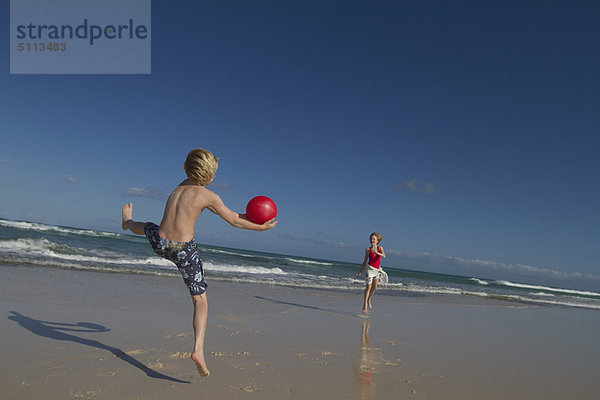 Kinder spielen mit rotem Ball am Strand