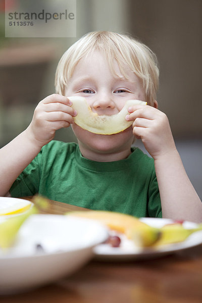 Junge spielt mit Melonenscheibe am Tisch