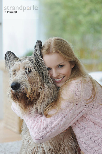 Lächelnde Frau umarmt Hund zu Hause