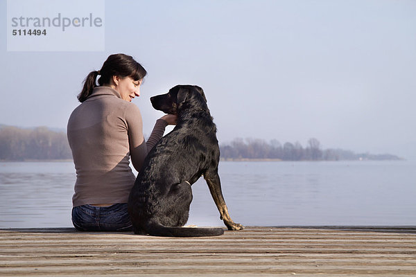 Frau sitzend mit Hund am Dock