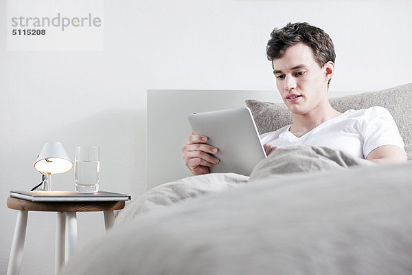 Mann mit Tablet-Computer im Bett