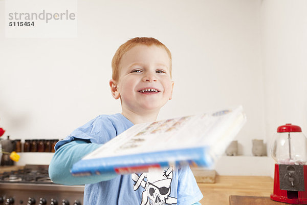 Lächelnder Junge mit Buch in der Küche