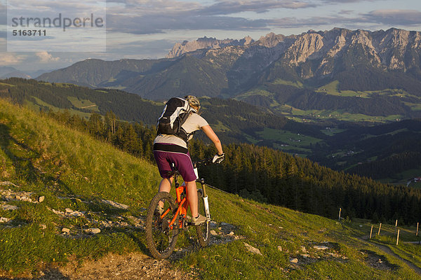 Österreich  Tirol  Spitzstein  Junge Frau Mountainbiken am Hang mit Kaisergebirge im Hintergrund