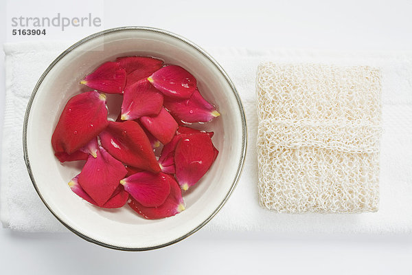 Nahaufnahme der Keramikschale mit Rosenblättern in Wasser und Schwamm auf Handtuch