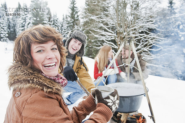 Österreich  Salzburger Land  Flachau  Junge Männer und Frauen sitzen am Kamin und kochen Tee im Schnee