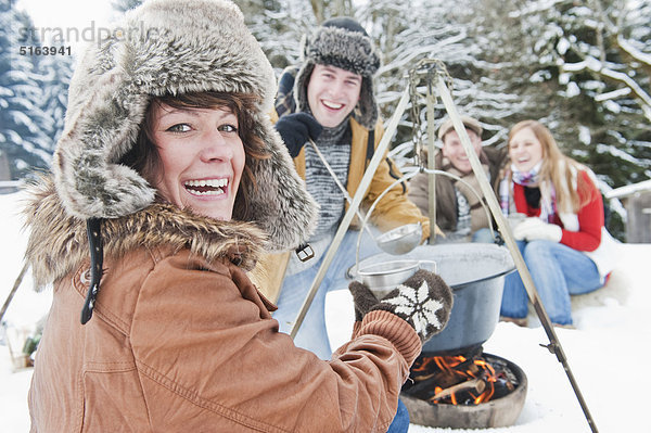 Österreich  Salzburger Land  Flachau  Junge Männer und Frauen sitzen am Kamin und kochen Tee im Schnee