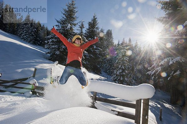 Österreich  Salzburger Land  Flachau  Junge Frau mit Schneeschuhen im Schnee springen