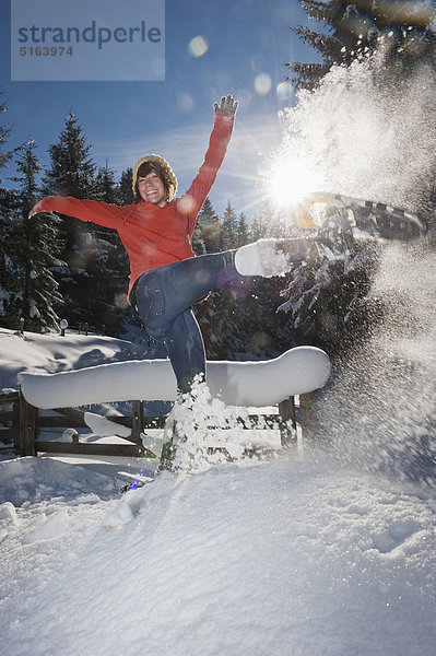 Österreich  Salzburger Land  Flachau  Junge Frau mit Schneeschuhen im Schnee springen