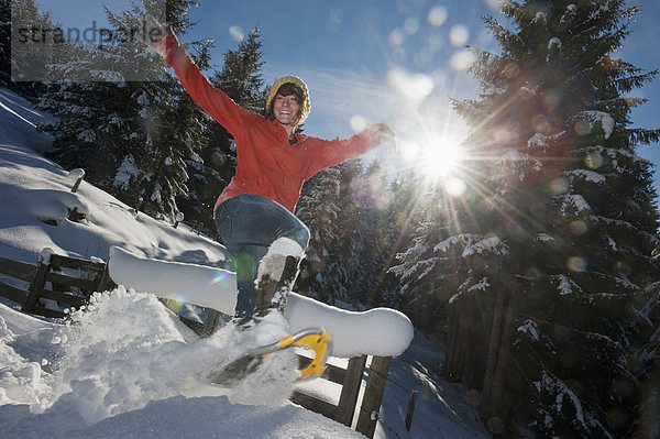 Österreich  Salzburger Land  Flachau  Junge Frau mit Schneeschuhen im Schnee springen