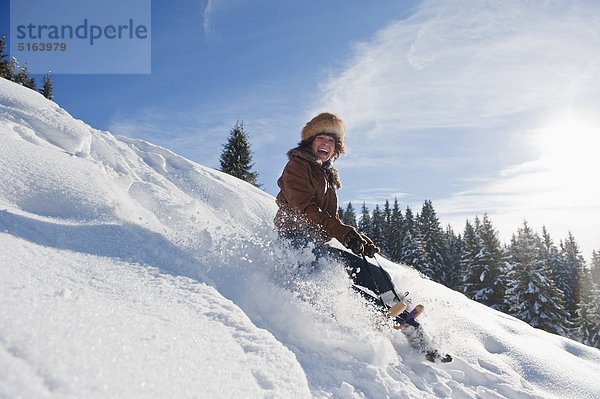 Österreich  Salzburger Land  Flachau  Junge Frau beim Rodeln im Schnee