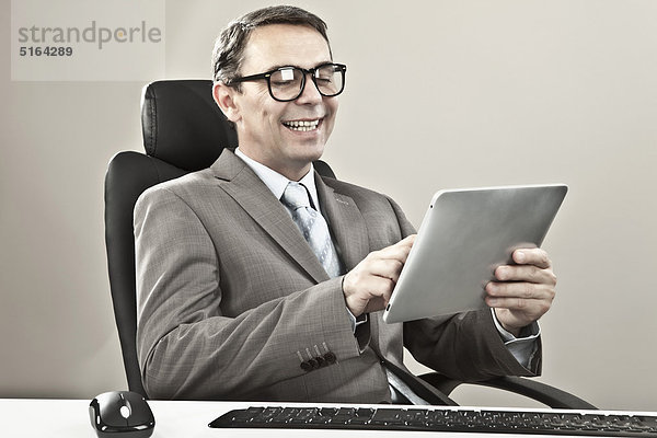 Geschäftsmann hält ipad und lächelt vor grauem Hintergrund