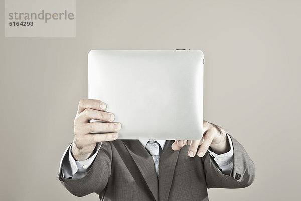 Nahaufnahme eines Geschäftsmannes  der das iPad vor seinem Gesicht vor grauem Hintergrund hält.