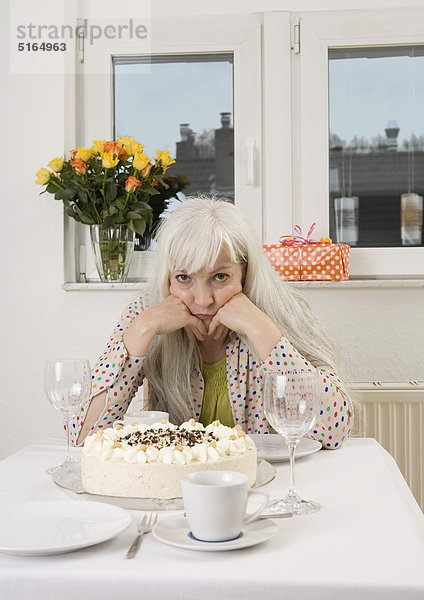 Frau am Esstisch sitzend mit Kuchen  Flowervase und Geschenk  Portrait