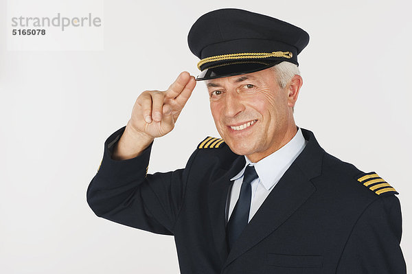 Nahaufnahme eines älteren Flugkapitäns  der vor weißem Hintergrund salutiert  lächelnd  Portrait