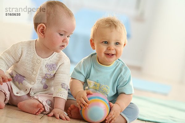 Zwei Babys sitzen auf dem Fußboden