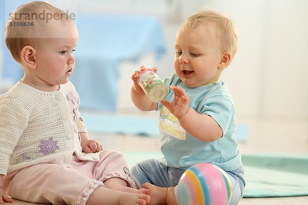 Zwei Babys sitzen auf dem Fußboden