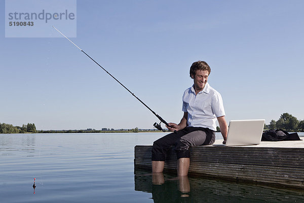 Mann beim Angeln und mit dem Laptop am Dock