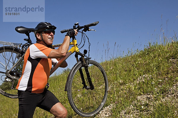 Mann mit Fahrrad auf grasbewachsenem Hang