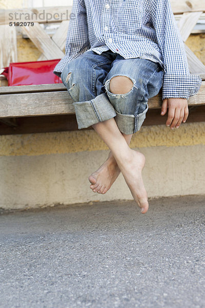 Nahaufnahme der nackten Füße des Jungen auf der Bank