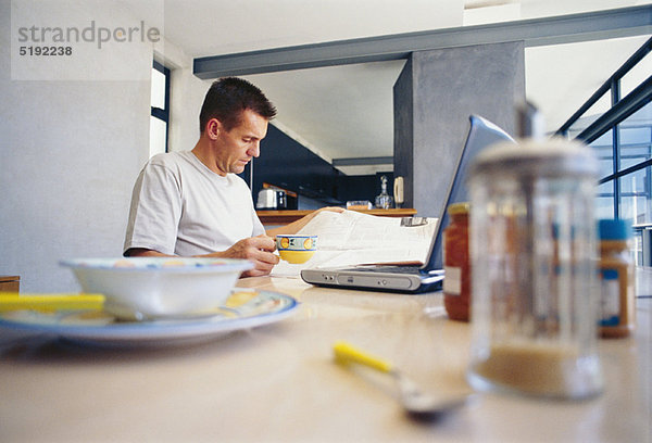 Mann mit Laptop beim Frühstück