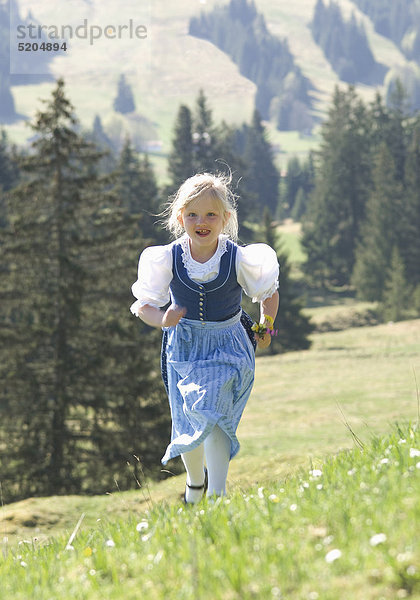 Kleines Mädchen rennt in Dirndl auf Bergwiese