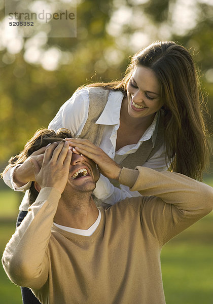 Paar in herbstlichem Park  sie hält ihm die Augen zu  lachen