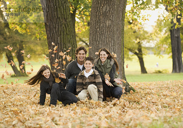 Familie in herbstlichem Park  hocken in Herbstlaub