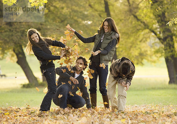 Familie in herbstlichem Park  werfen mit Herbstlaub