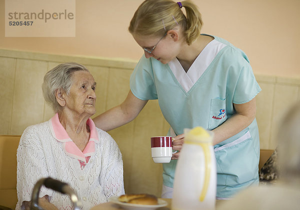 Altenheim  Pflegerin bringt Seniorin eine Tasse