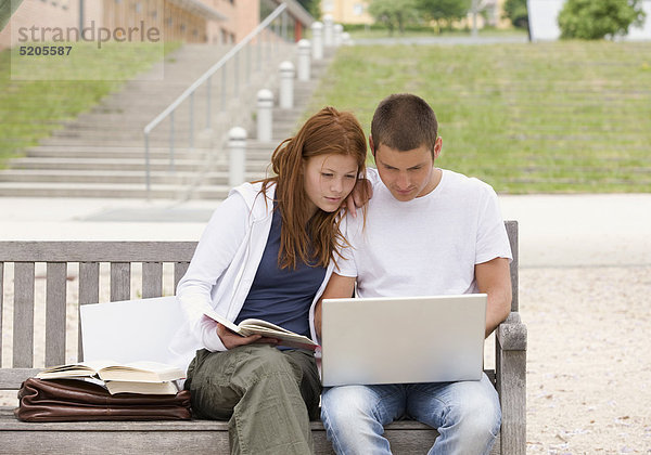 Schülerpaar mit Laptop und Büchern auf Bank