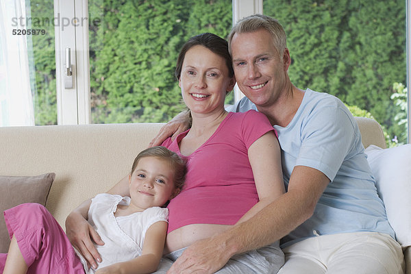 Schwangere sitzt mit Mann und Tochter auf Sofa