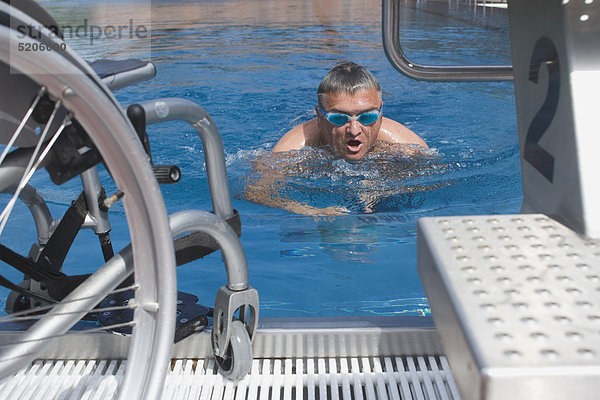 Behindertensport  Mann schwimmt im Schwimmbecken  Rollstuhl steht am Rand