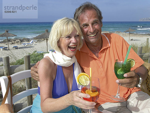 Älteres Paar sitzt mit Cocktails an Strandbar