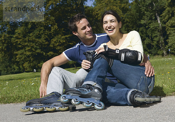 Paar  sitzen mit Inlineskates auf Weg  lachen