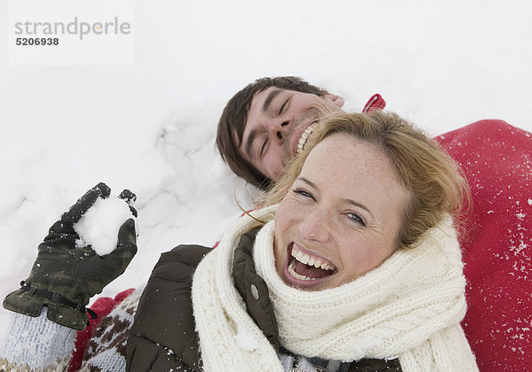 Paar im Winter  liegen lachend im Schnee