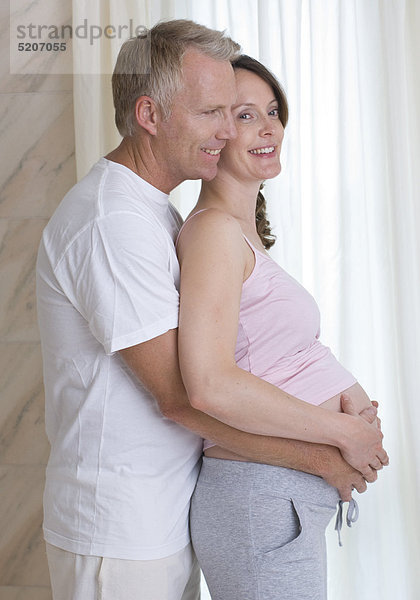 Mann umfasst von hinten den Bauch von schwangerer Frau