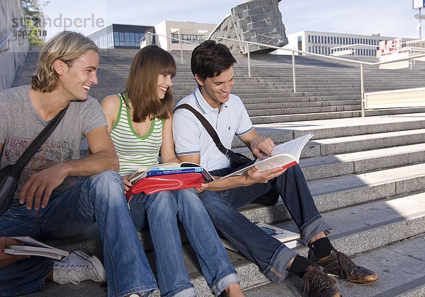 Zwei Studenten und Studentin sitzen auf Treppe  lachen