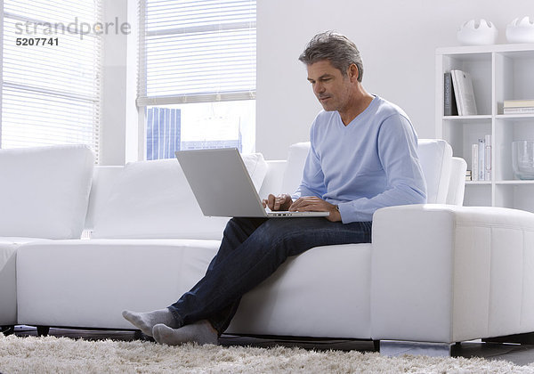 Mann sitzt zu Hause mit Laptop auf Sofa