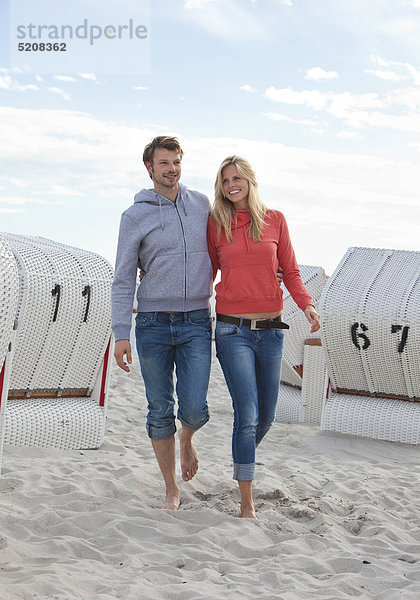 Paar läuft im Sand zwischen Strandkörben