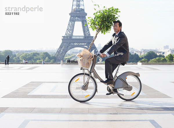 Geschäftsmann mit einer Pflanze auf einem Fahrrad mit dem Eiffelturm im Hintergrund  Paris  Ile-de-France  Frankreich