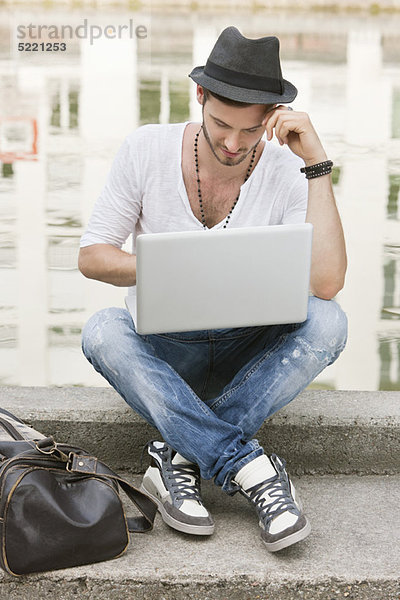 Mann  der auf dem Sims eines Kanals sitzt und einen Laptop benutzt  Paris  Ile-de-France  Frankreich