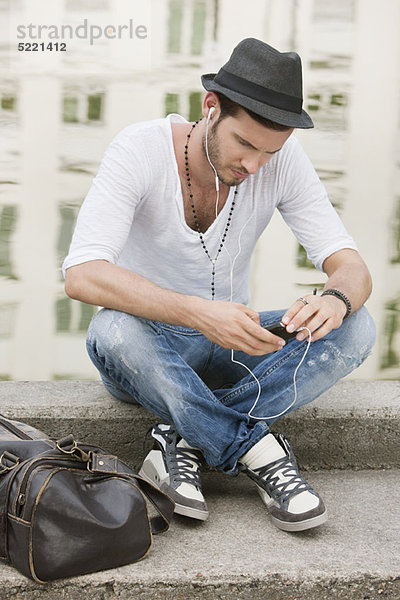 Mann sitzt auf dem Felsvorsprung eines Kanals und hört Musik mit einem MP3-Player  Paris  Ile-de-France  Frankreich