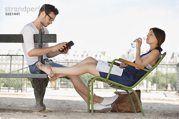 Frau trinkt Wasser und ihr Mann mit einem digitalen Tablett  Jardin des Tuileries  Paris  Ile-de-France  Frankreich