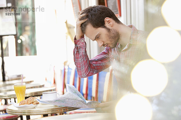Mann  der an einem Straßencafé sitzt und eine Karte liest  Paris  Ile-de-France  Frankreich
