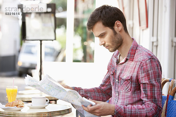 Mann  der an einem Straßencafé sitzt und eine Karte liest  Paris  Ile-de-France  Frankreich