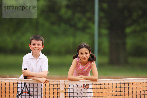 Caucasian Boy und Girl Posing By Net In Tennisplatz