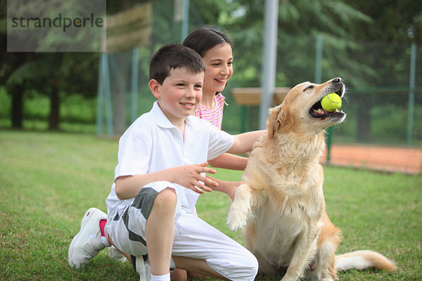 Jungen Jungen und Mädchen spielen mit Labrador Hund Holding Tennisball