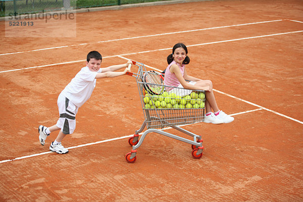 Junge Mädchen In Trolley mit voller Tennisbälle drücken