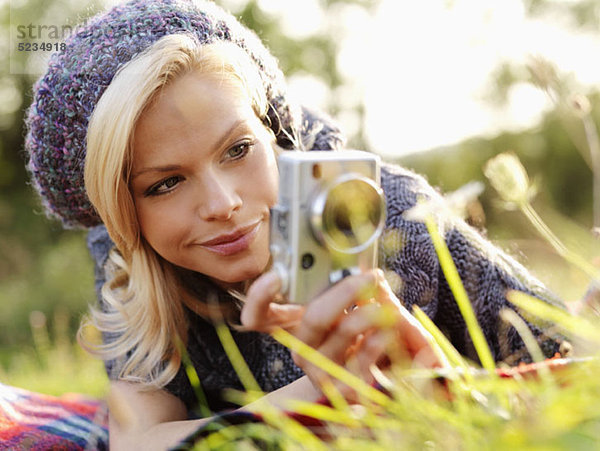 Eine Frau beim Fotografieren im Gras liegend